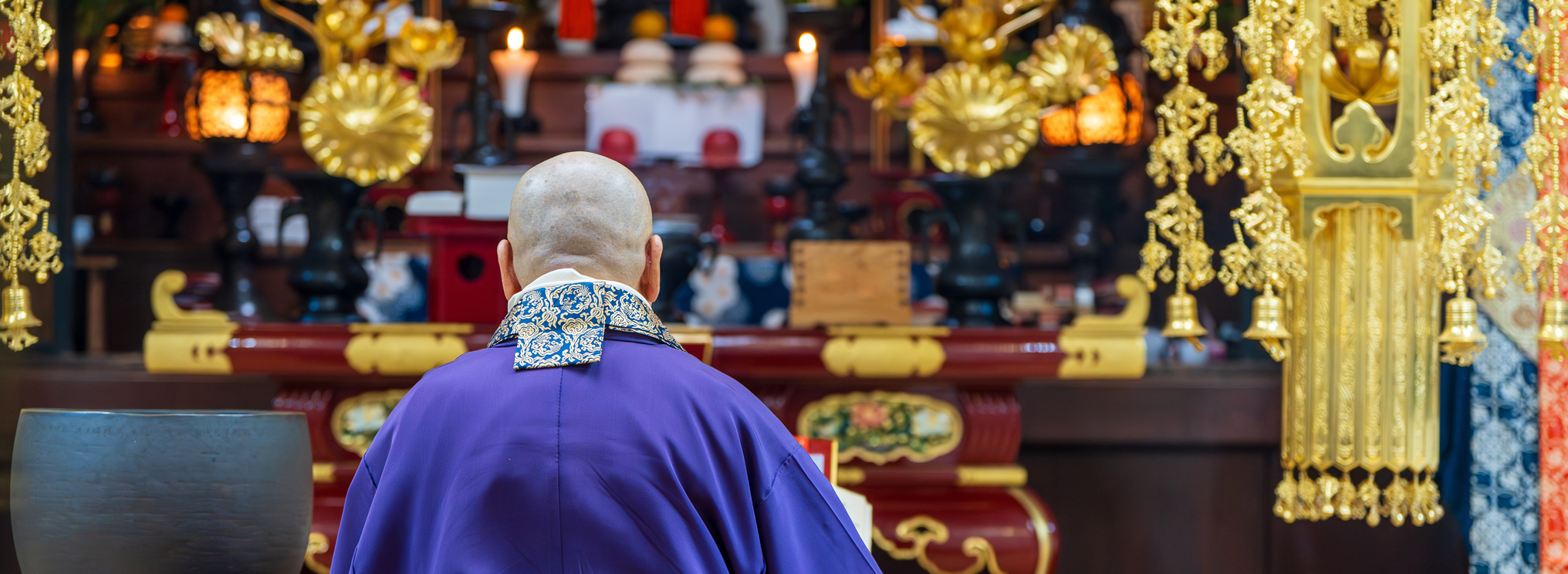 Ein buddhistischer Mönch in purpurfarbenem Gewand in einem Tempel als Symbol für rituelle Andacht, Achtsamkeit und den spirituellen Umgang mit Tod und Wiedergeburt im Buddhismus.