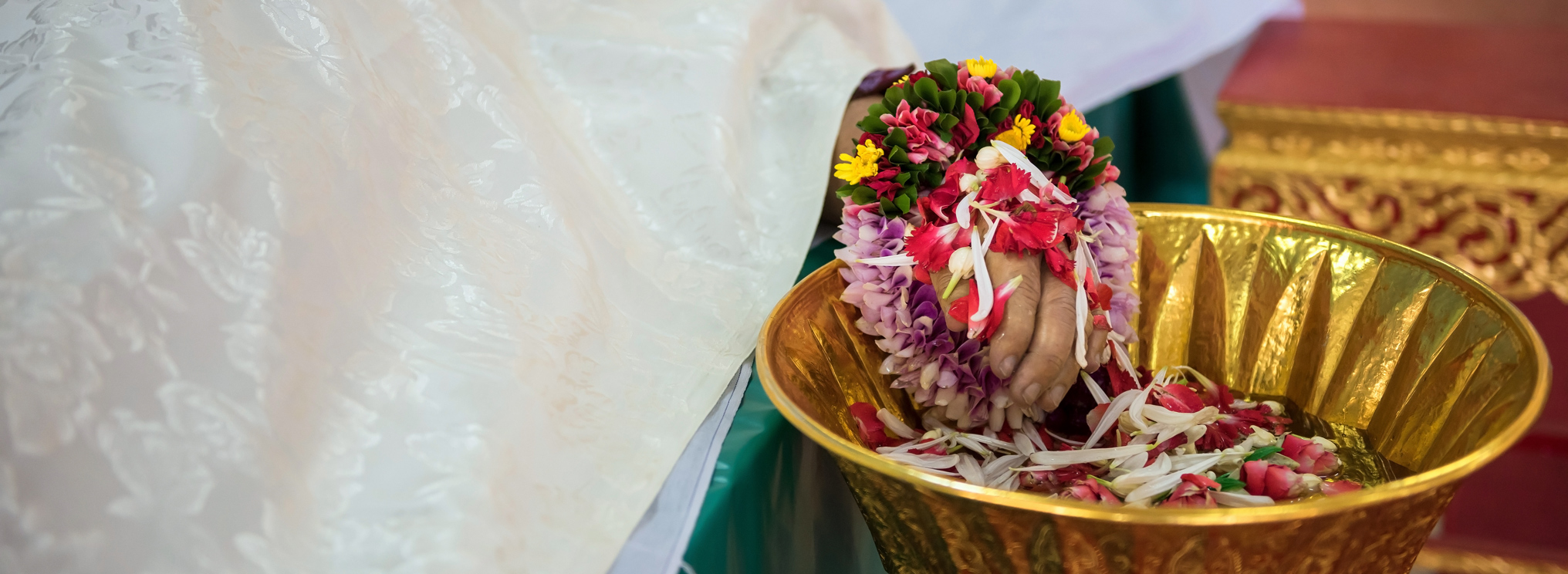 Eine mit Blumen verzierte Hand legt Blüten in eine goldene Schale – Ausdruck für Opfergaben, Mitgefühl und den achtsamen Umgang mit Tod und Vergänglichkeit im Buddhismus.